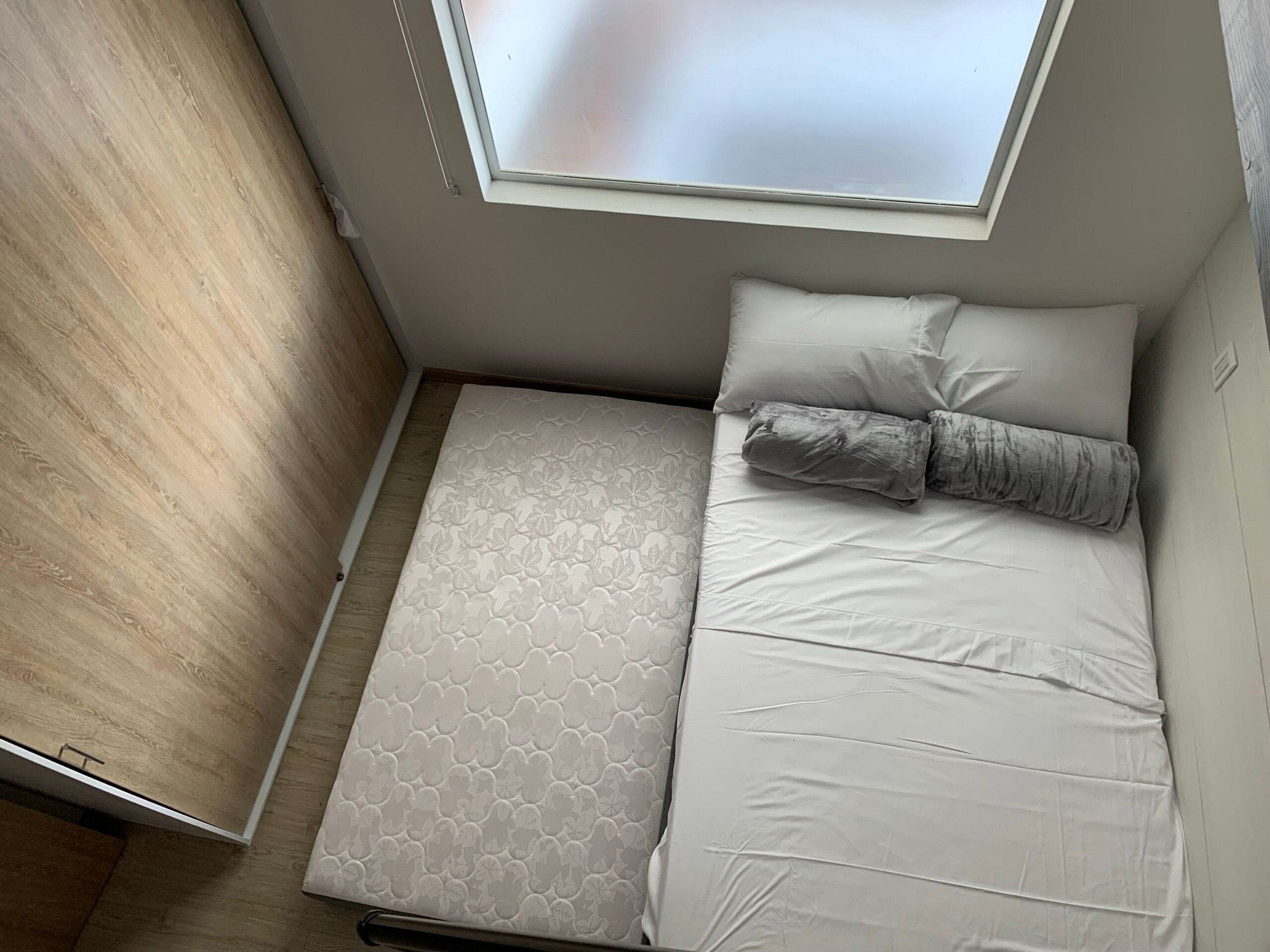 Ein kleines Zimmer mit Bett, Fenster und Holzboden.