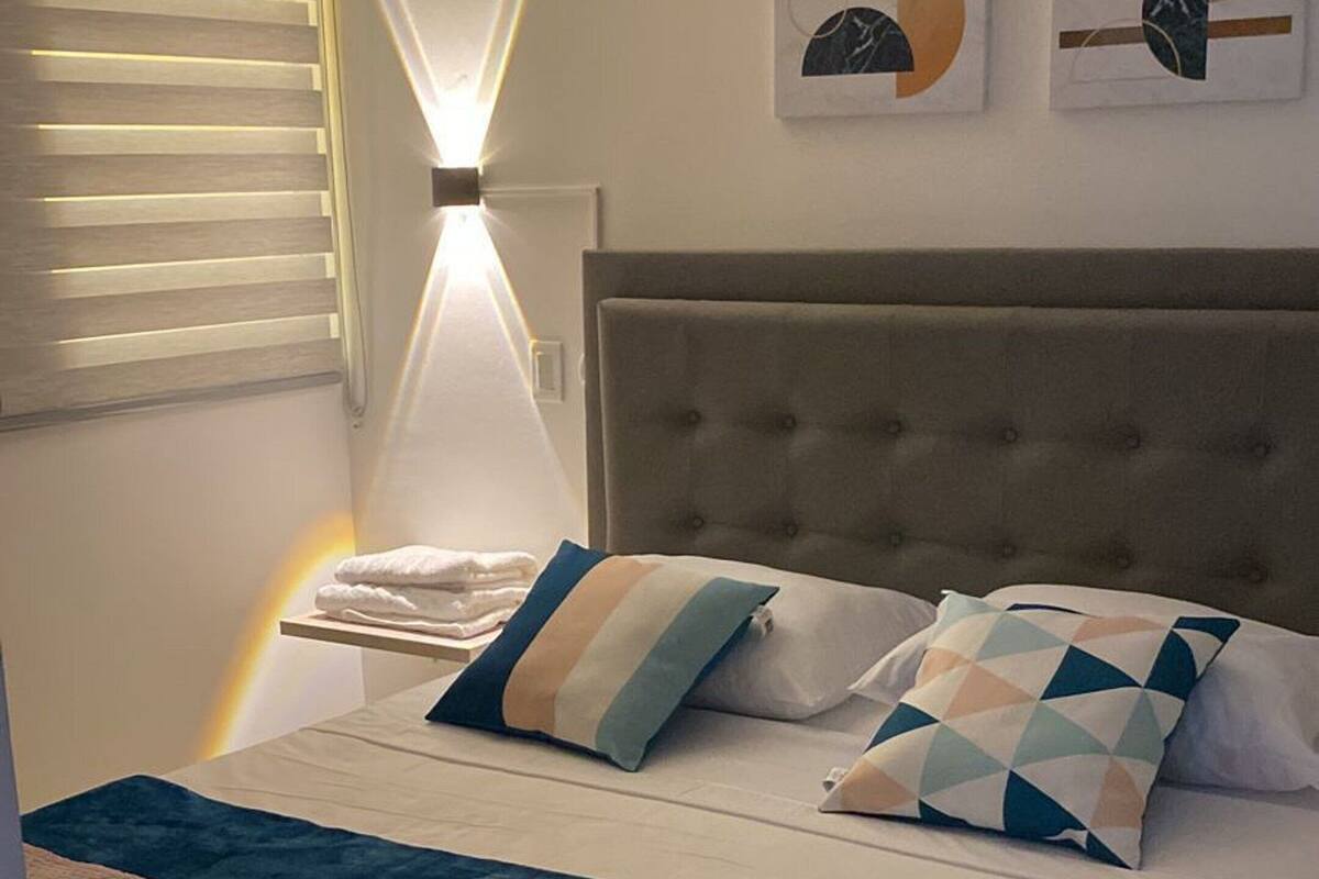 Une chambre à coucher avec un lit, des oreillers, une table de chevet, une lampe et des œuvres d’art abstraites accrochées au mur.