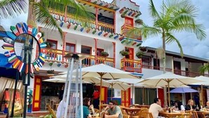 An outdoor dining area with wooden tables and chairs, umbrellas, and a decorative windmill. - Edificio Avenida Malecon (Guatapé)