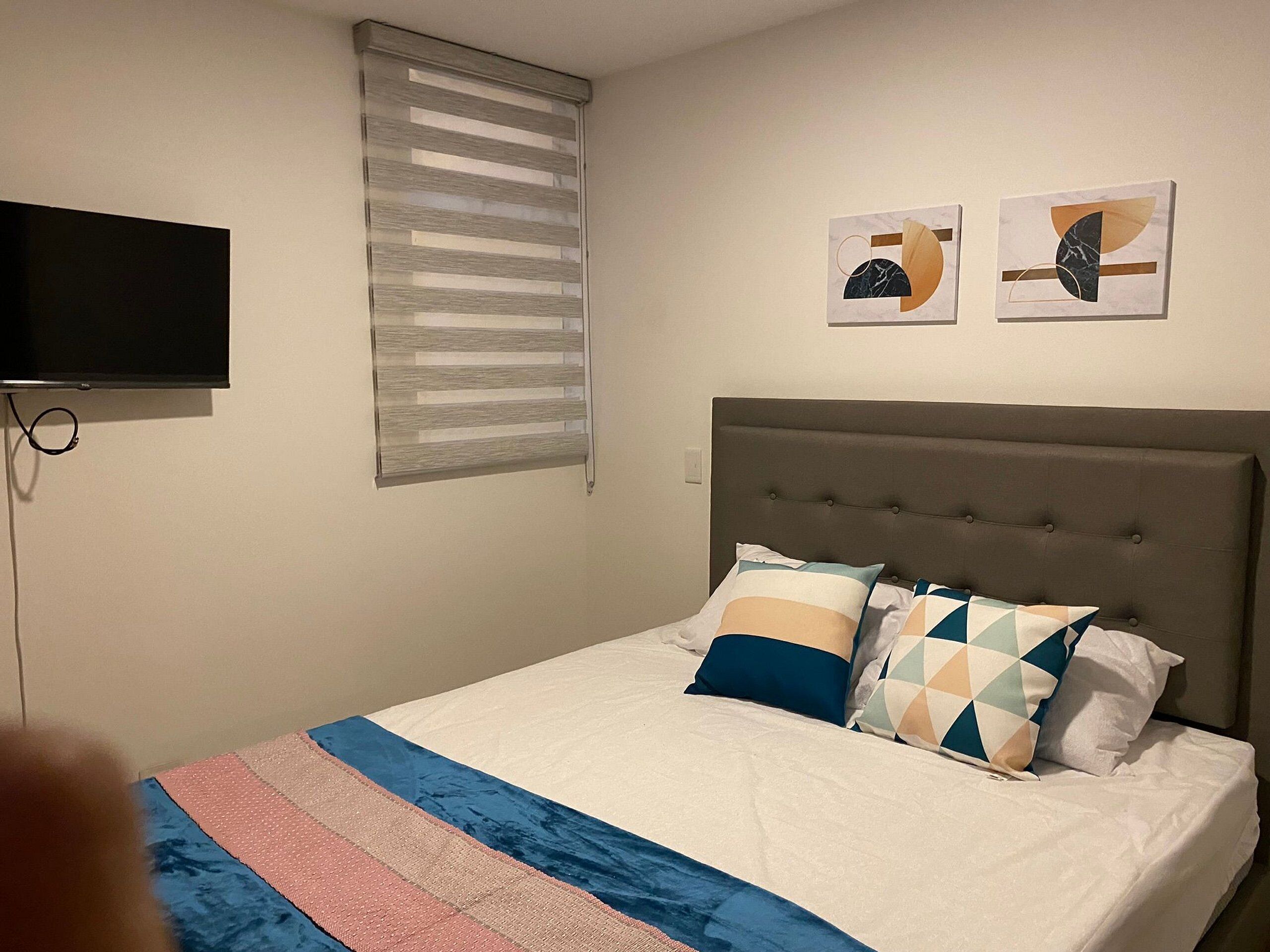 Una camera da letto con un letto, una televisione a parete e due dipinti astratti.