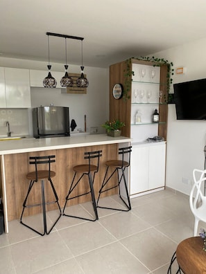 Una cocina moderna con una isla central, taburetes de bar, un refrigerador y un televisor montado en la pared.