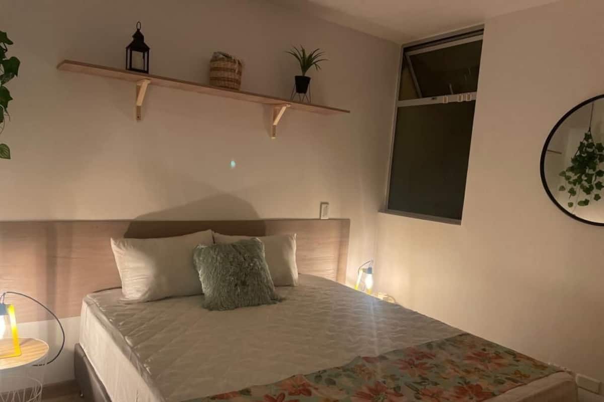 Une chambre à coucher comprenant un lit, une table de chevet, une étagère murale décorative et une fenêtre.