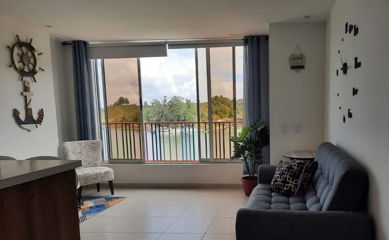 A living room with a view of a balcony, a sofa, a chair, and a small table.