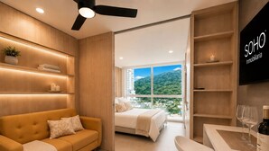 A modern hotel room with a sofa, a bed, a dining area, and a TV.
