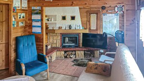 Ein gemütliches Interieur einer Holzhütte mit einem blauen Sessel, einer Couch, einem Kamin, einem Fernseher und einer Holzwand, die mit Kalendern und einem Willkommensschild verziert ist.