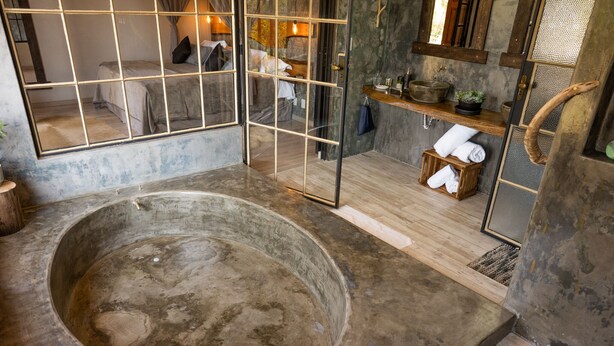 A rustic bathroom with a large bathtub, wooden shelves, and a mirror.