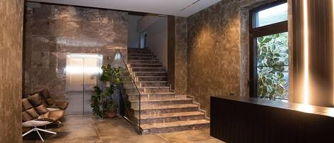 A modern interior with a stone wall, a staircase, a reception desk, and a seating area with chairs.