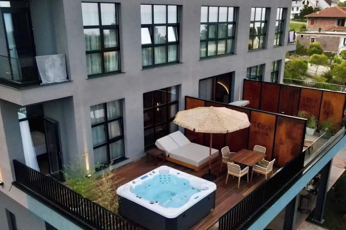 Un balcon extérieur moderne doté d’un jacuzzi, d’un espace salon et d’un grand parasol.