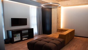 A modern living room with a flat-screen TV, a dark entertainment unit, a brown sofa, and a unique circular light fixture. - Toka Hotel Restaurant (Udënisht)