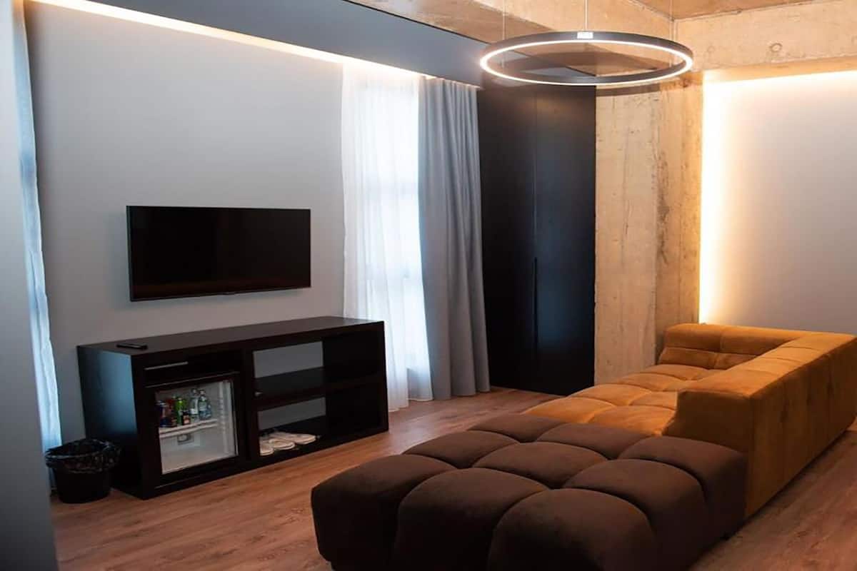 Un salon moderne doté d’un téléviseur à écran plat, d’un meuble de rangement sombre, d’un canapé marron et d’un luminaire circulaire original.