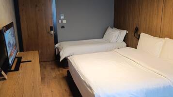A modern hotel room with two beds, a wooden desk, a TV, and a ceiling light fixture.