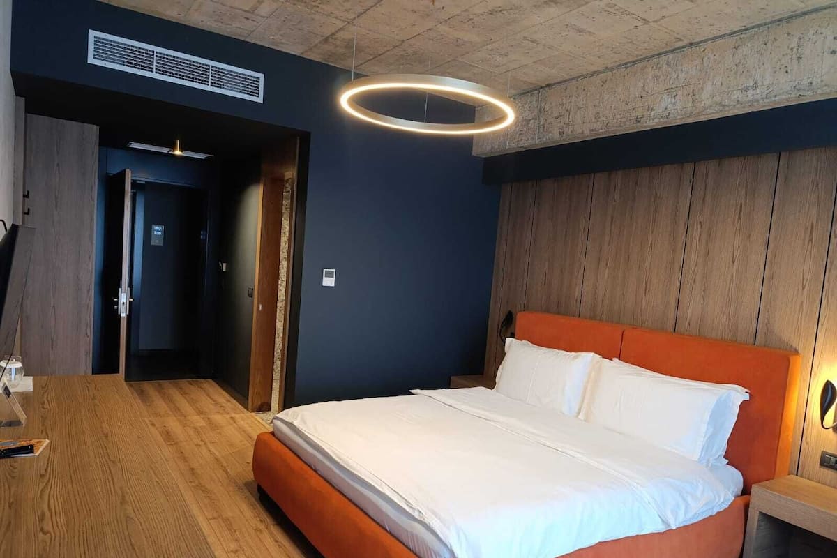 Une chambre d’hôtel moderne dotée d’un grand lit, d’un plancher en bois et d’un luminaire circulaire original.