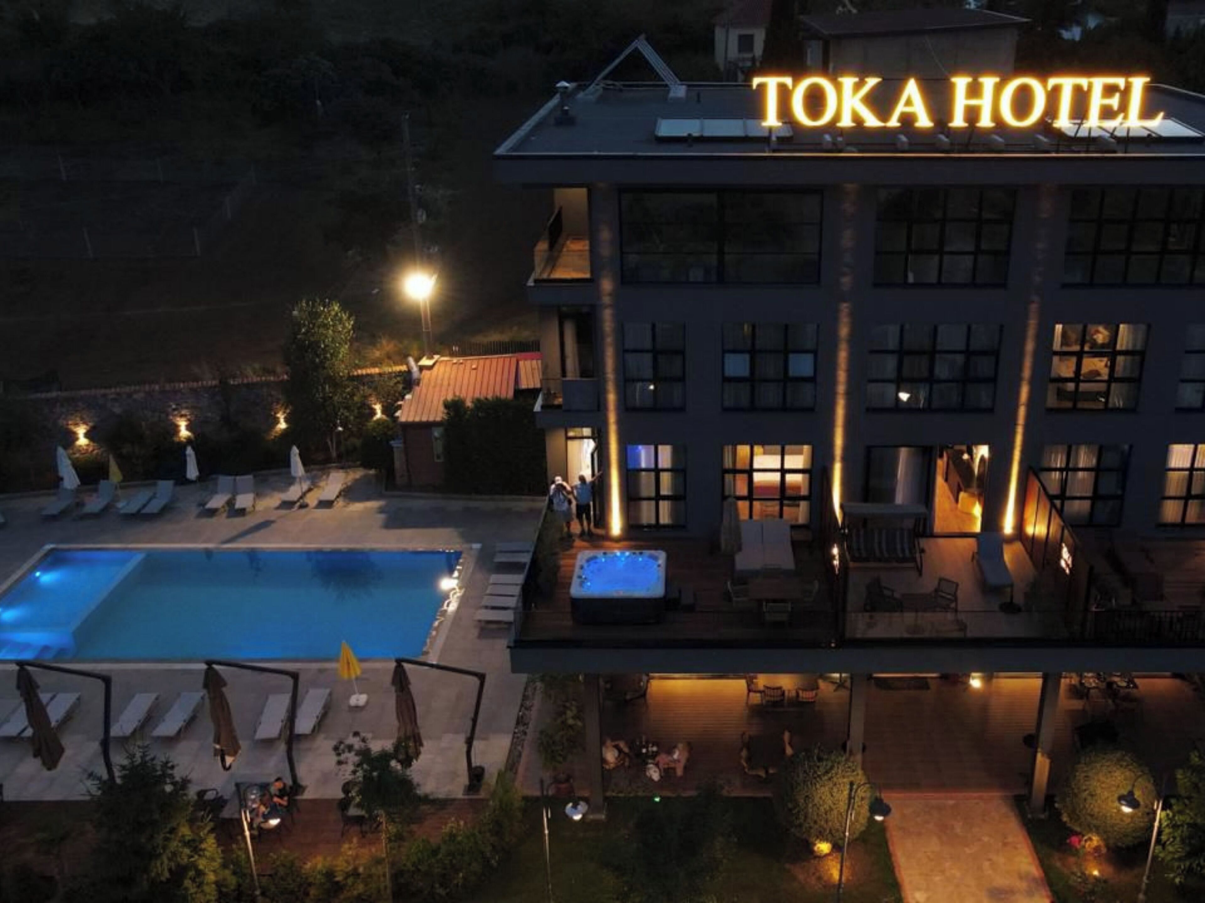 A hotel with a swimming pool, outdoor seating, and a well-lit facade.