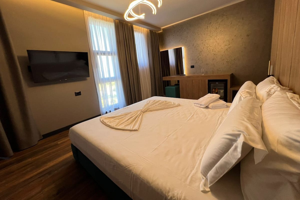 Une chambre d’hôtel comprenant un lit, un téléviseur à écran plat fixé au mur, une table de chevet en bois et un miroir.