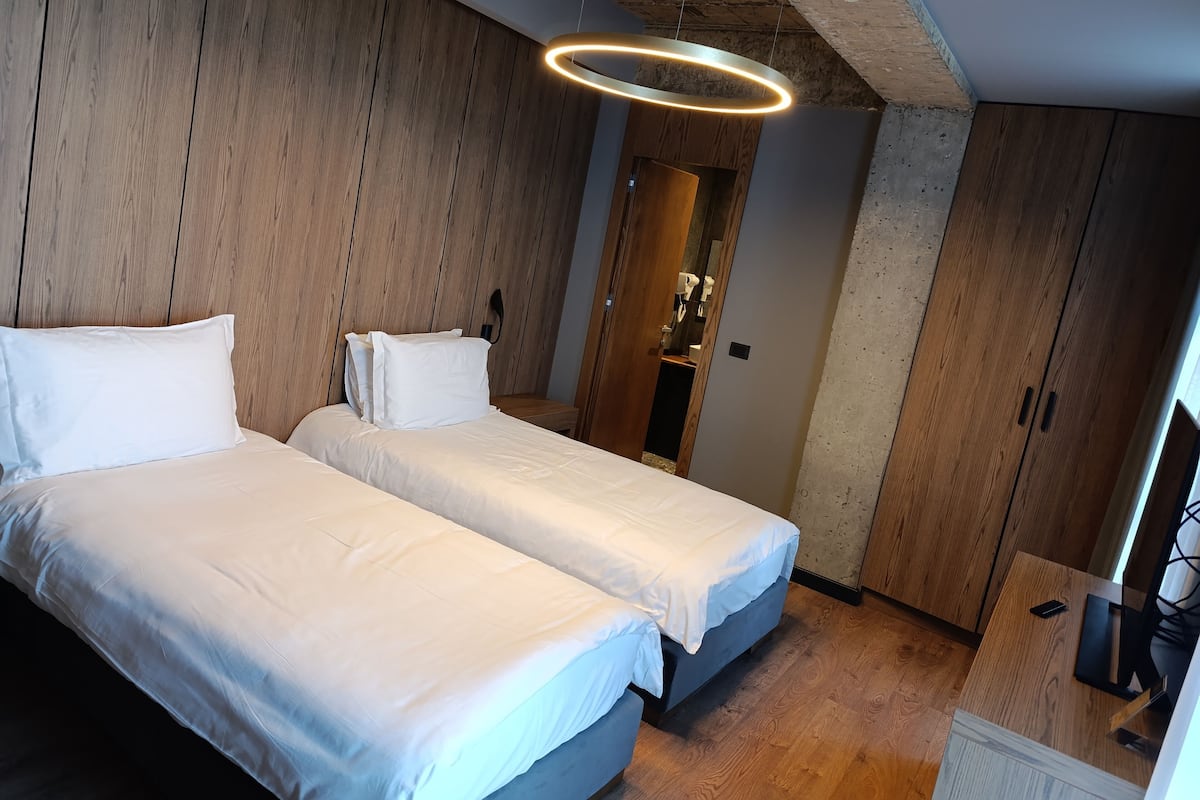 Une chambre avec deux lits, des murs recouverts de panneaux en bois, un luminaire moderne et une armoire en bois.
