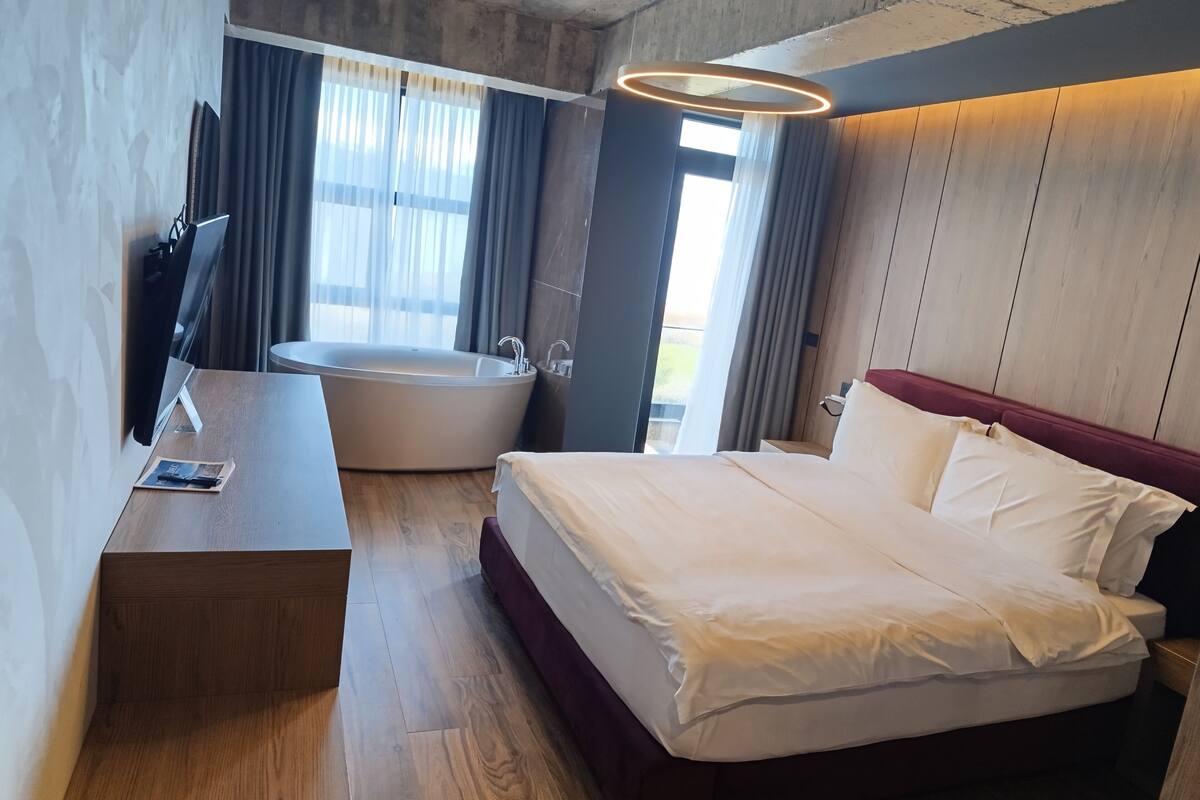 Une chambre d’hôtel moderne avec un grand lit, une baignoire et un bureau avec une chaise.