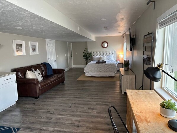 A spacious room with a large bed, a brown leather couch, a wooden desk, and a TV mounted on the wall.