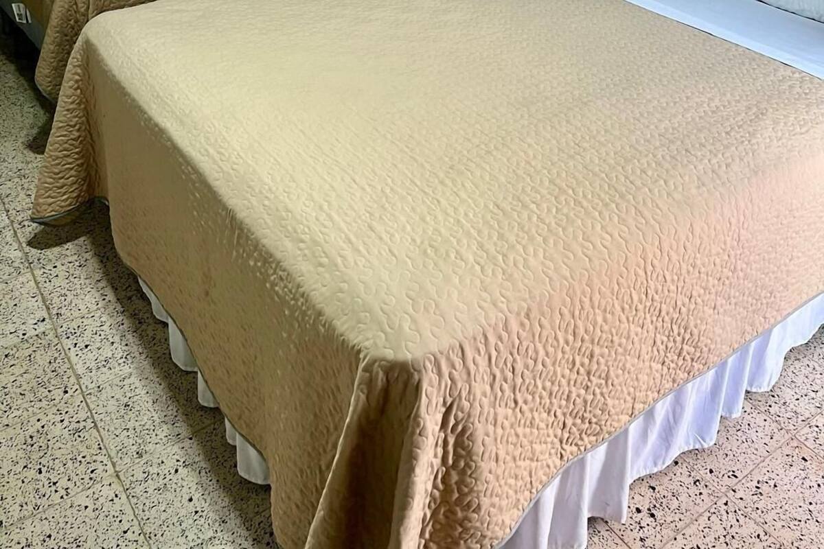 Two single beds with beige and white bedding in a room with plain walls and a tiled floor.