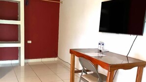 A room with a wooden desk, a chair, a TV mounted on the wall, and a red door. - APARTA HOTEL PALMEROLA (Comayagua)