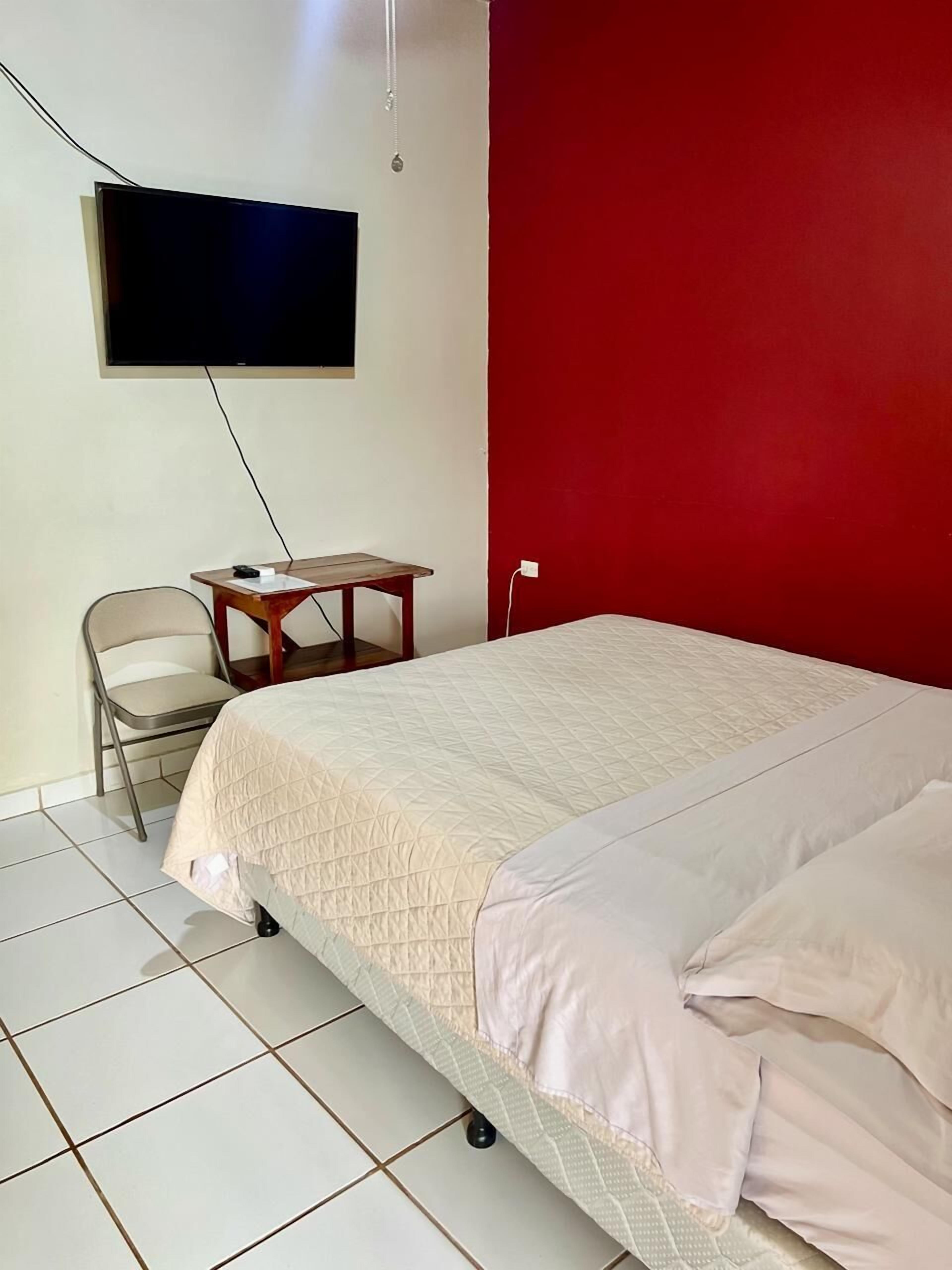 A room with a bed, a chair, a small table, and a TV mounted on the wall.
