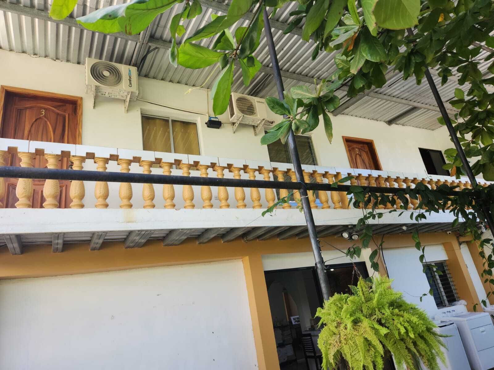 Un edificio con balcón, aire acondicionado y planta colgante.