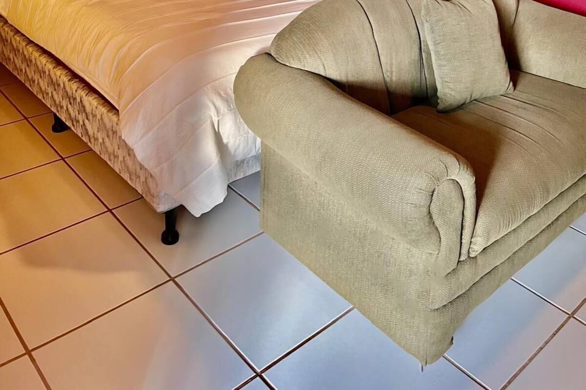 A bed with a white bedspread and pillows, a beige sofa, and a red wall.