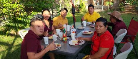 Un grupo de personas cenando al aire libre en una mesa con una sombrilla grande.