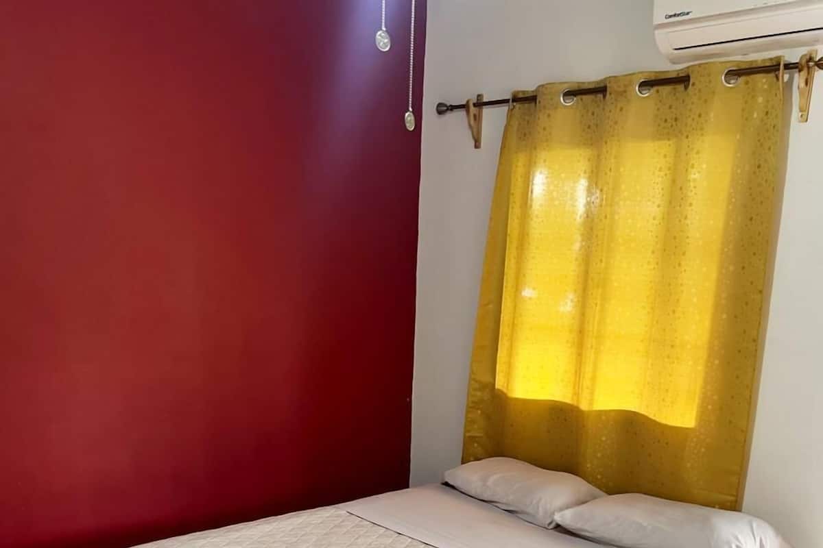 A single-bed room with a red wall, a yellow curtain, and a white tiled floor.
