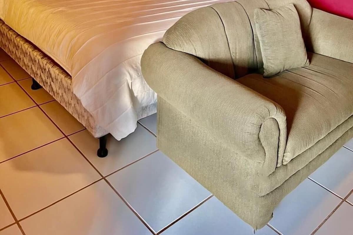 A bed with white bedding, a beige armchair, and a red wall.