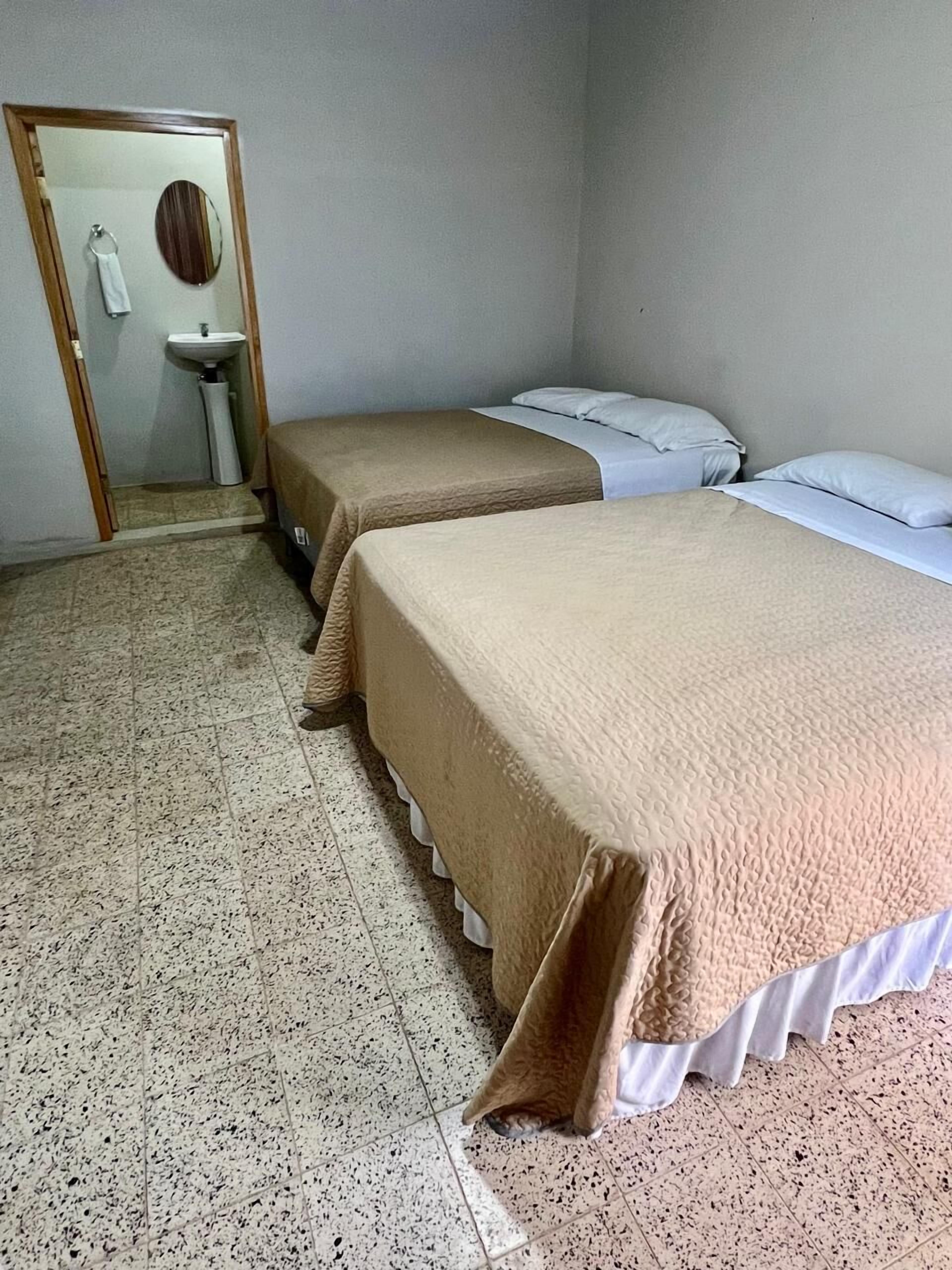 A small, simple room with two beds, a sink, and a mirror.