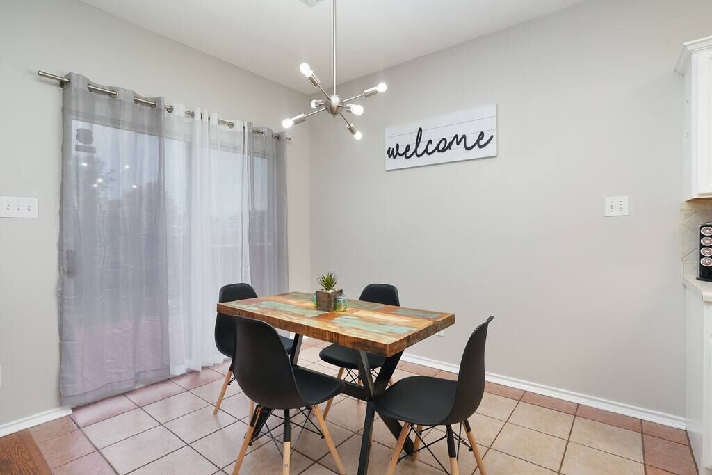Un comedor con una mesa de madera, sillas negras, un letrero que dice 'welcome' y una lámpara de araña moderna.