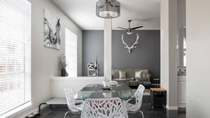 Un comedor moderno con una mesa de vidrio y sillas blancas, un ventilador de techo y una cabeza de ciervo montada en la pared.