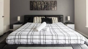 Un dormitorio con una cama grande, dos mesitas de noche, un cabecero y una obra de arte colgada en la pared.