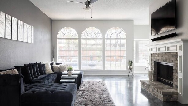 Una sala moderna con un sofá de color oscuro, una chimenea y ventanas grandes con vistas al exterior.