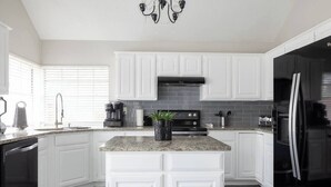 Una cocina moderna con armarios blancos, encimera de granito, refrigerador negro y una araña.