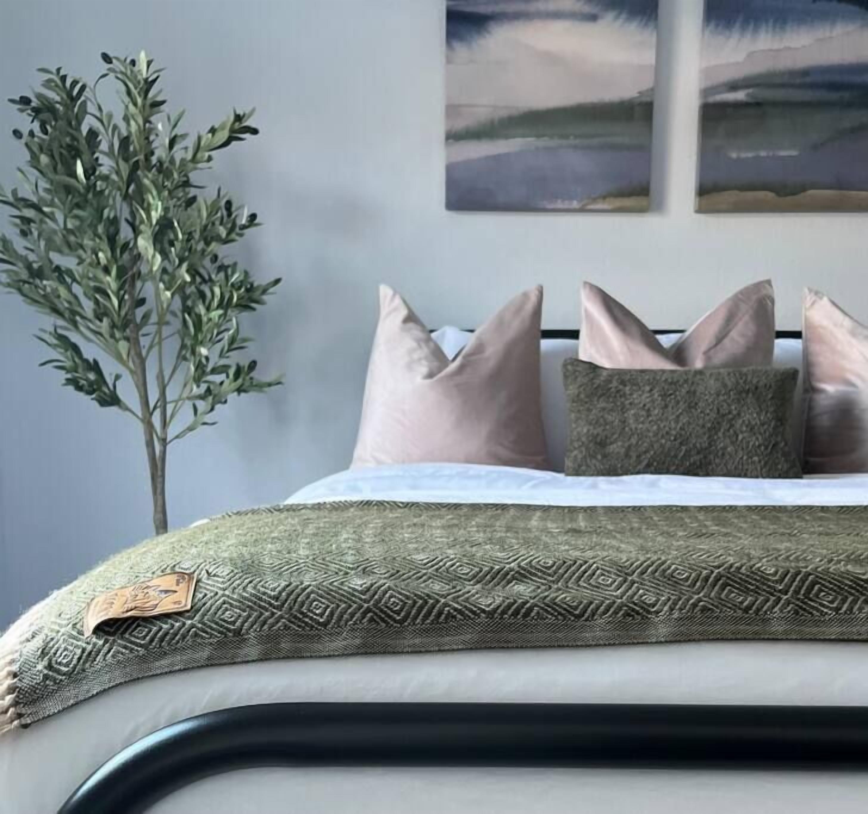 A neatly made bed with a patterned bedspread, a decorative pillow, and a view of a landscape painting on the wall.