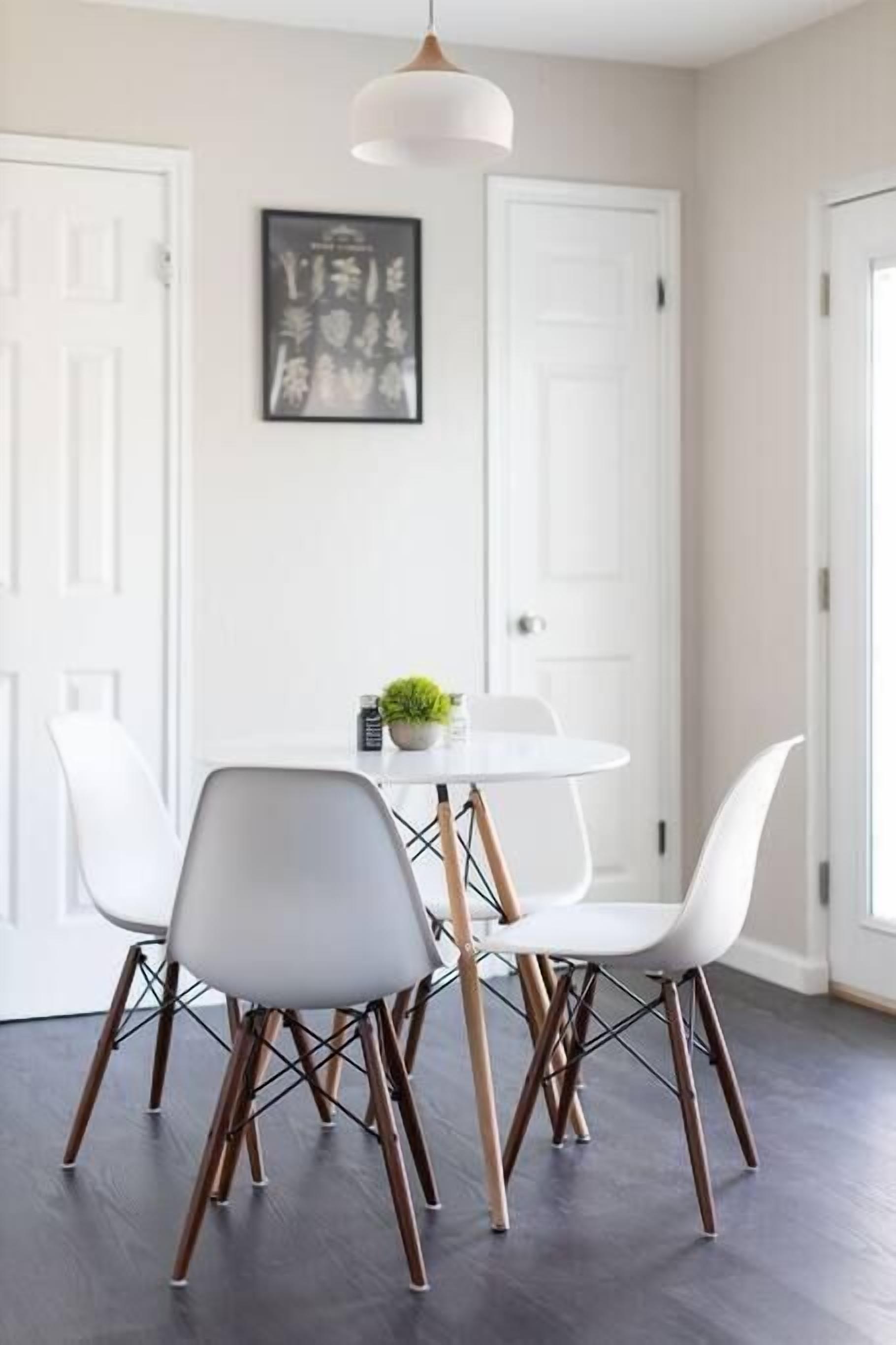 Uma área de refeições com uma mesa redonda, cadeiras brancas e uma luminária pendente.