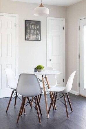 A dining area with a round table, white chairs, and a pendant light.