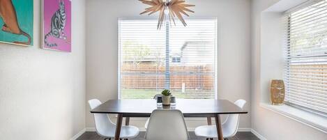 A dining area with a table, chairs, a pendant light, and artwork on the wall.