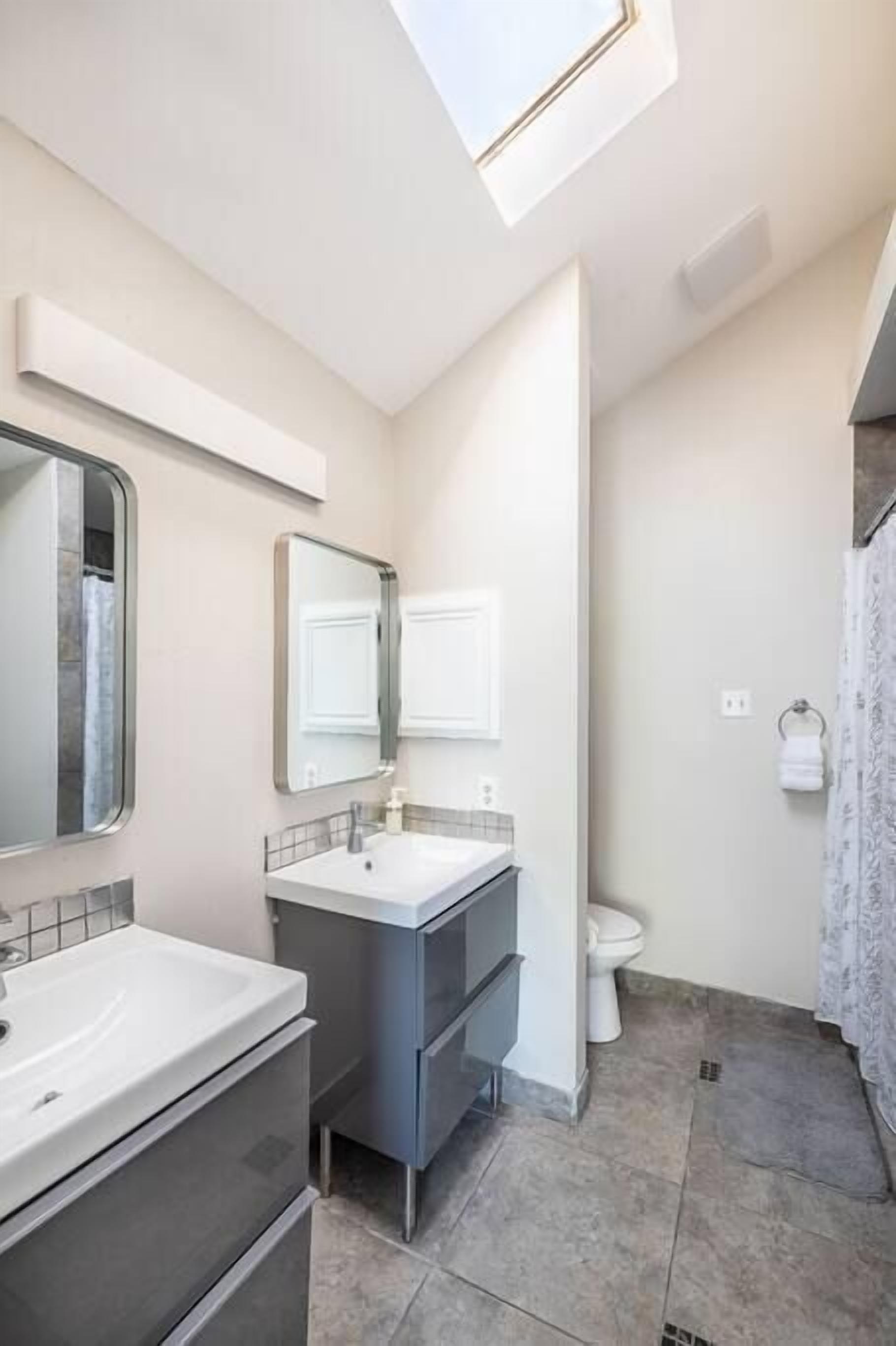 Un baño moderno con tragaluz, un espejo grande, un lavabo blanco, tocador y retrete.