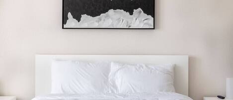 A modern hotel room with a large bed, white bedding, and a black and white abstract painting above the bed.