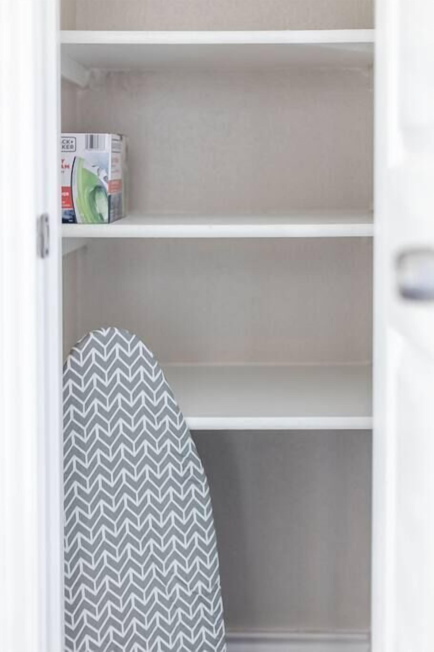 Une étagère blanche sur laquelle se trouve une boîte de mouchoirs verts et un fer à repasser à motifs gris et blancs.
