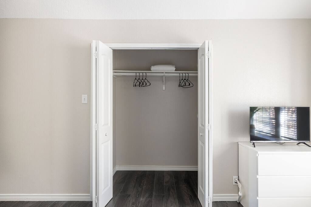 Une chambre dotée d’un dressing, avec une commode blanche, un téléviseur à écran plat et un plancher en bois.