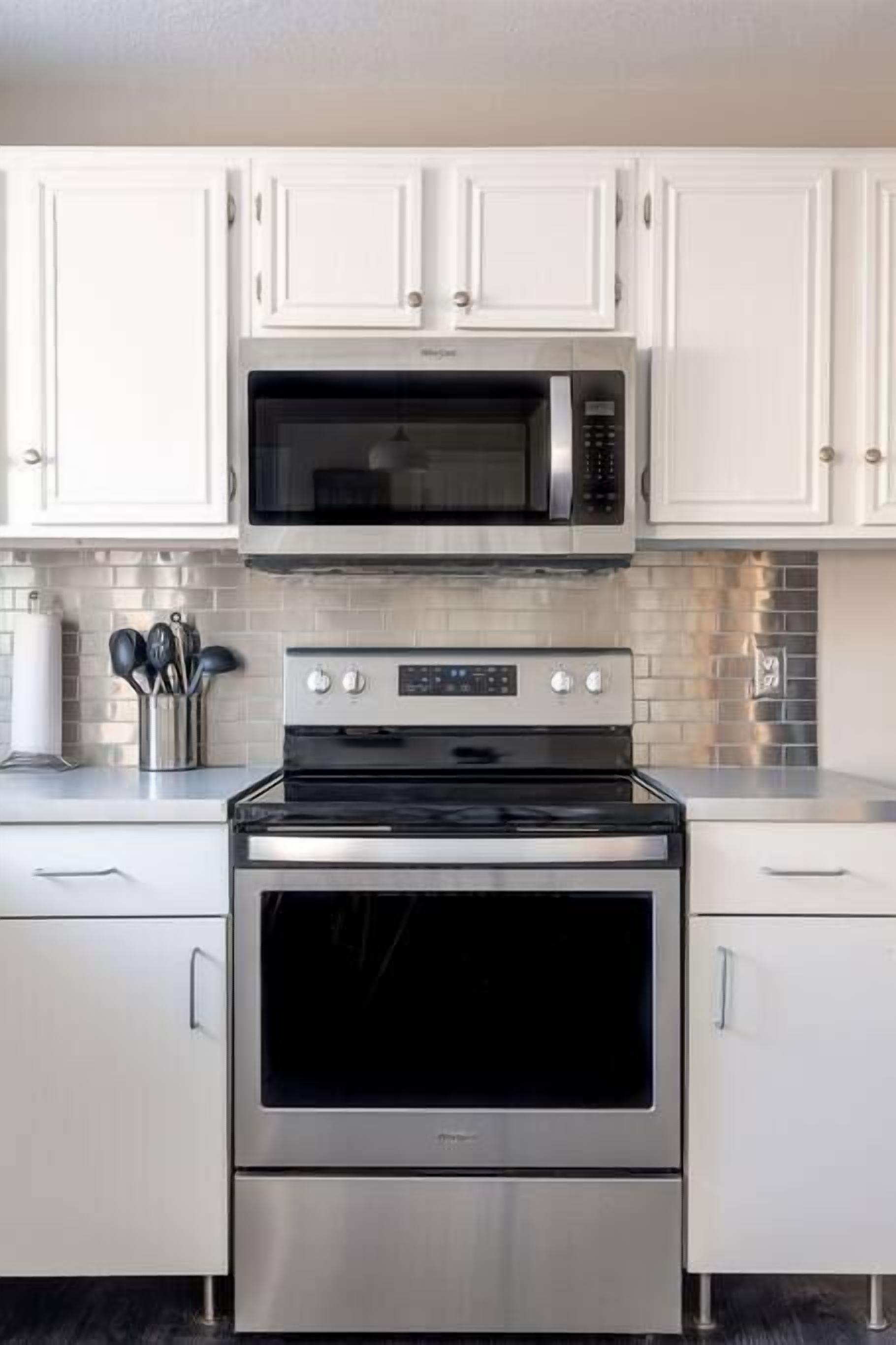 A kitchen with white cabinets, a stainless steel microwave, and an oven.