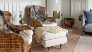 Una habitación acogedora con sillas de mimbre, un reposapiés blanco, una planta de cactus y una olla de cobre.