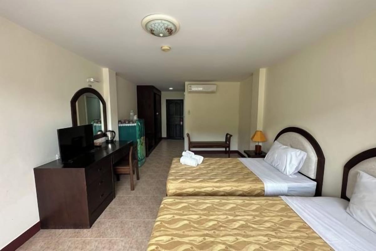 A hotel room with two beds, a desk with a mirror, a television, and an air conditioning unit.
