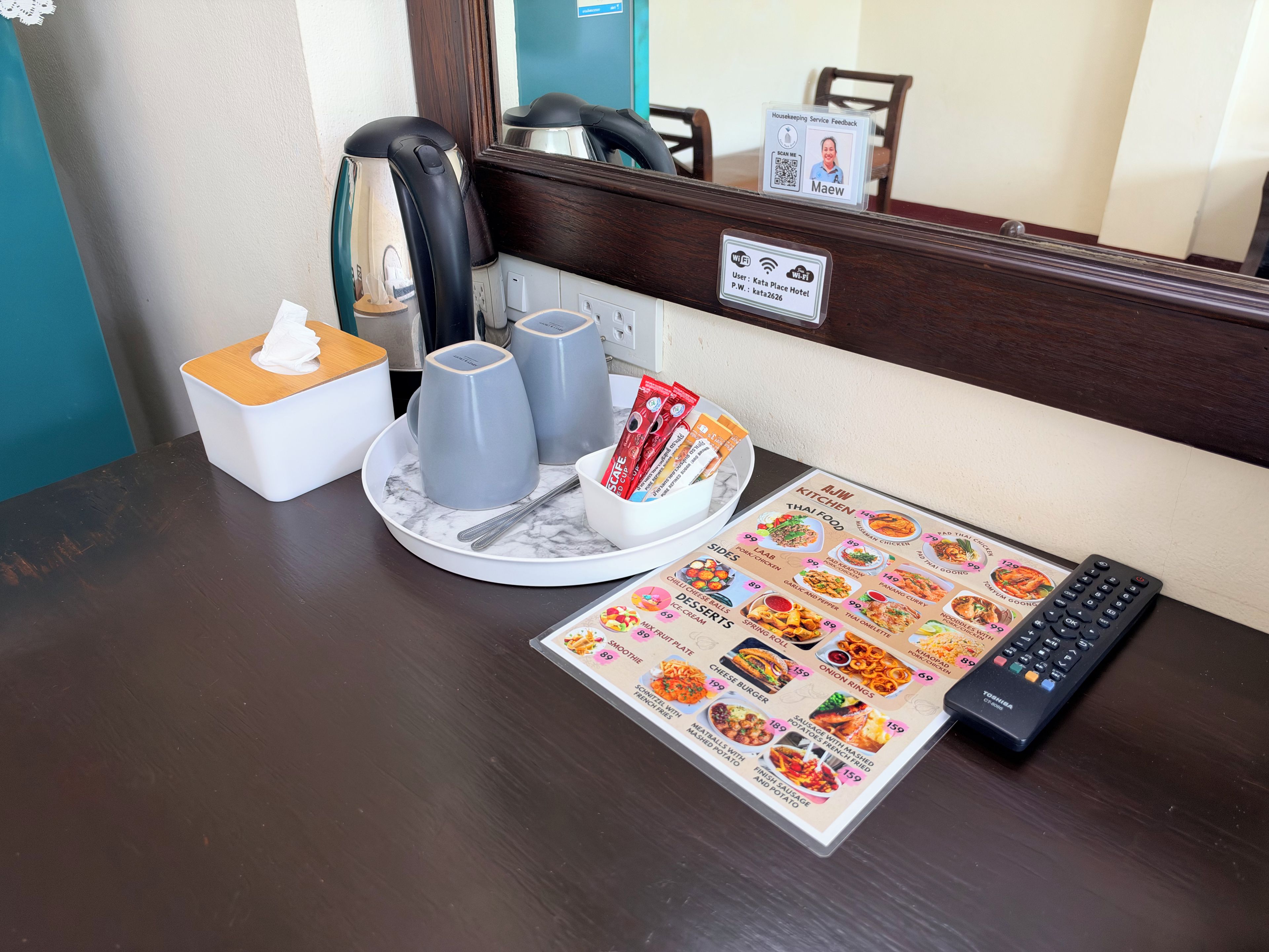 Une chambre d’hôtel avec une table à manger, un menu, une télécommande et une boîte de mouchoirs.
