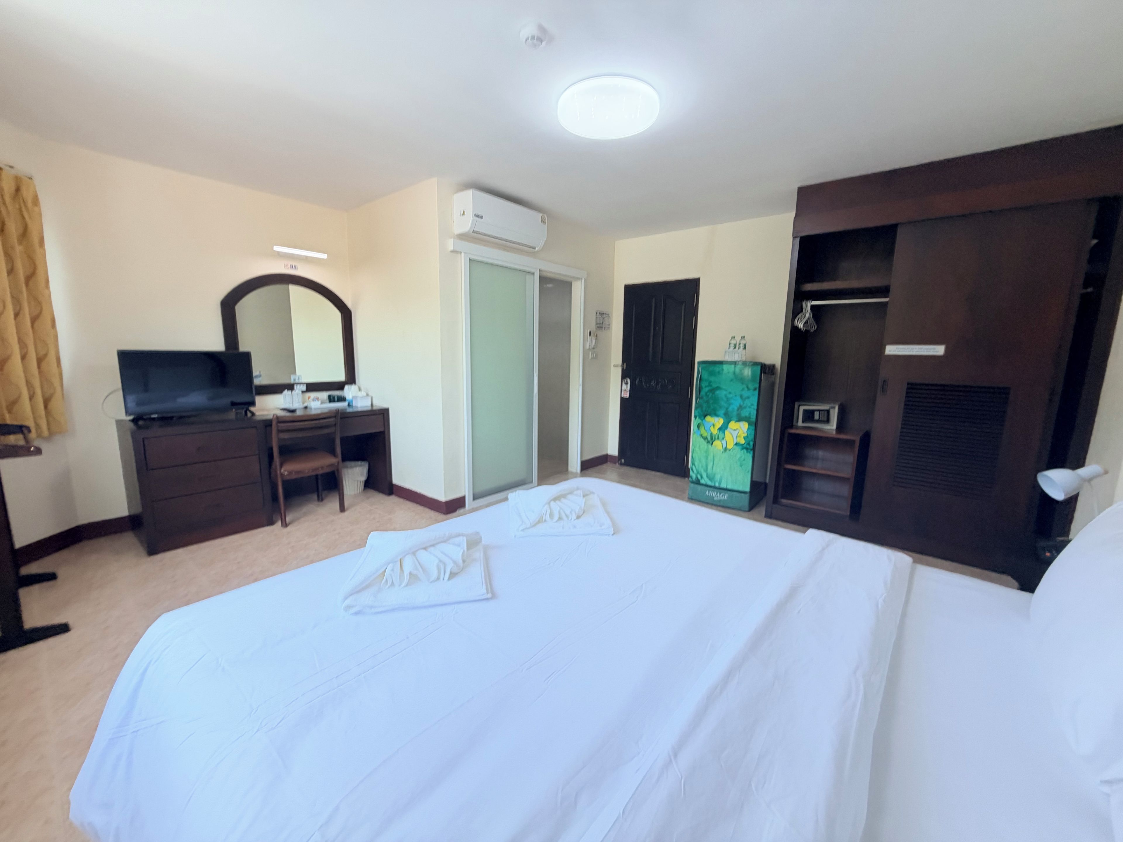 A hotel room with a bed, a desk with a computer, a wardrobe, and a minibar.