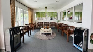 A spacious room with a large dining table surrounded by wooden chairs, a standing heater, and a large window with curtains. - Kata Place Hotel (Karon)