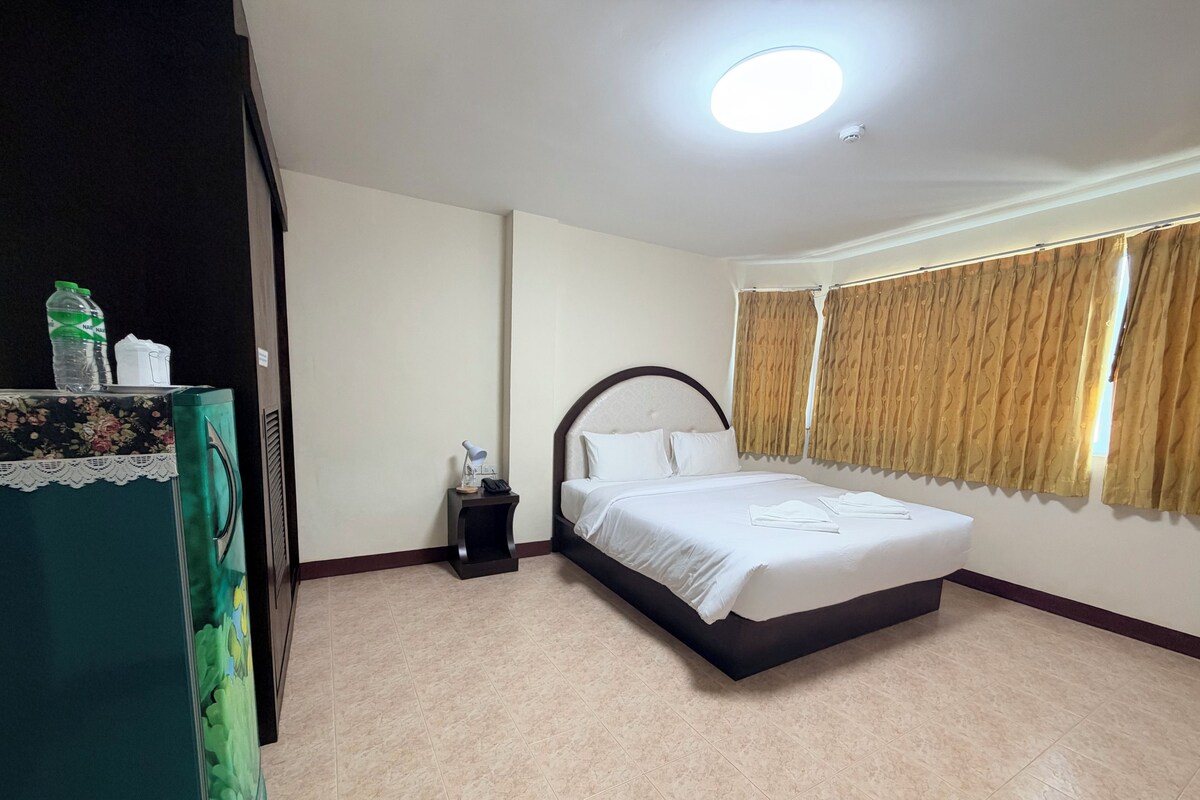 A hotel room with a bed, bedside table, lamp, and curtains.
